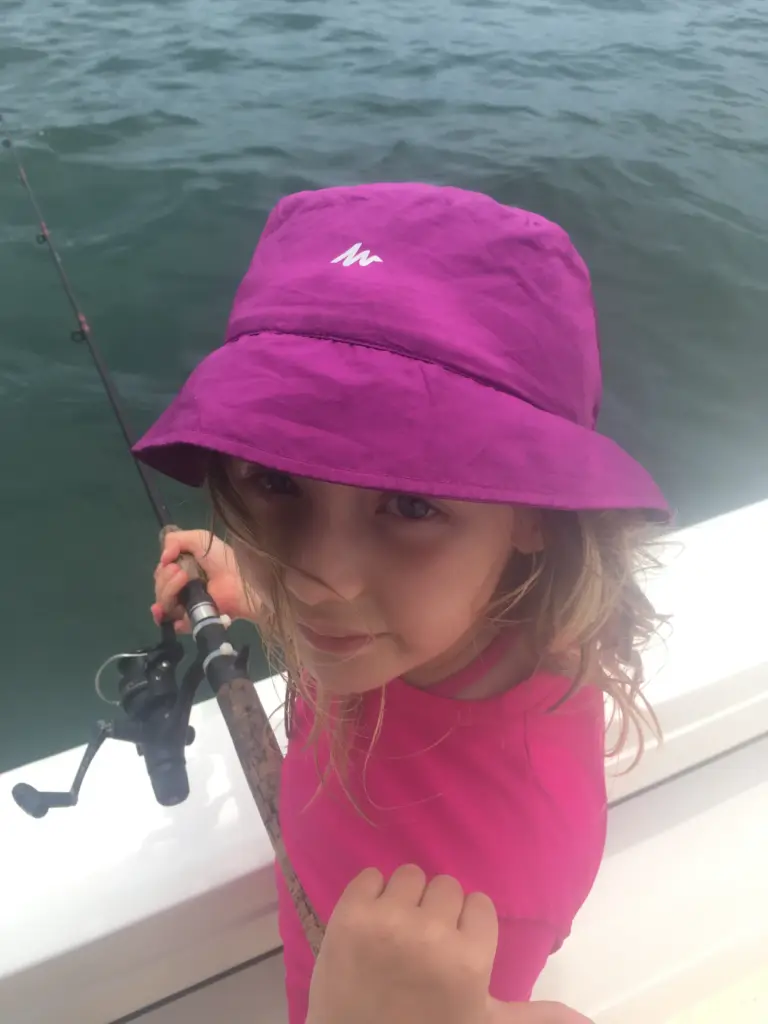 A young guest in a sun hat holds a fishing rod on a family trip from Playa Garza.