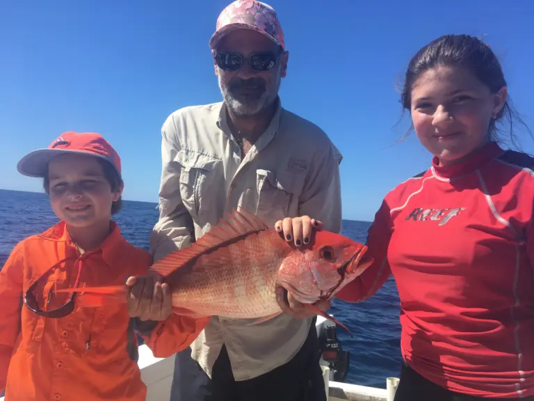 A grandfather and his two grandchildren hold a snapper caught on a family trip from Nosara.