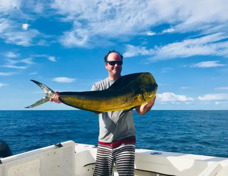 A guest holds a mahi-mahi on the boat under a clear blue sky off Nosara.
