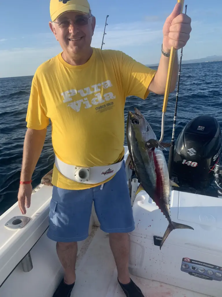 A guest in a pura vida shirt gives a thumbs up with a tuna caught off Playa Garza.