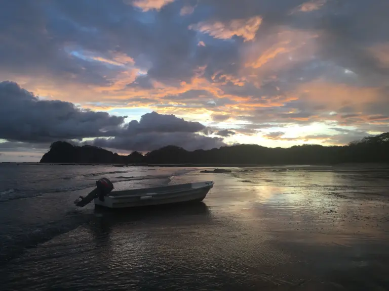 The fishing boat rests on the sand at Playa Garza under a dramatic sunset sky.