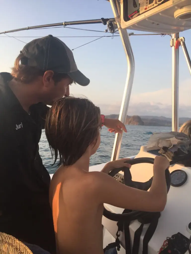 Captain Juri points out the coast to a young guest at the helm as the sun sets off Nosara.