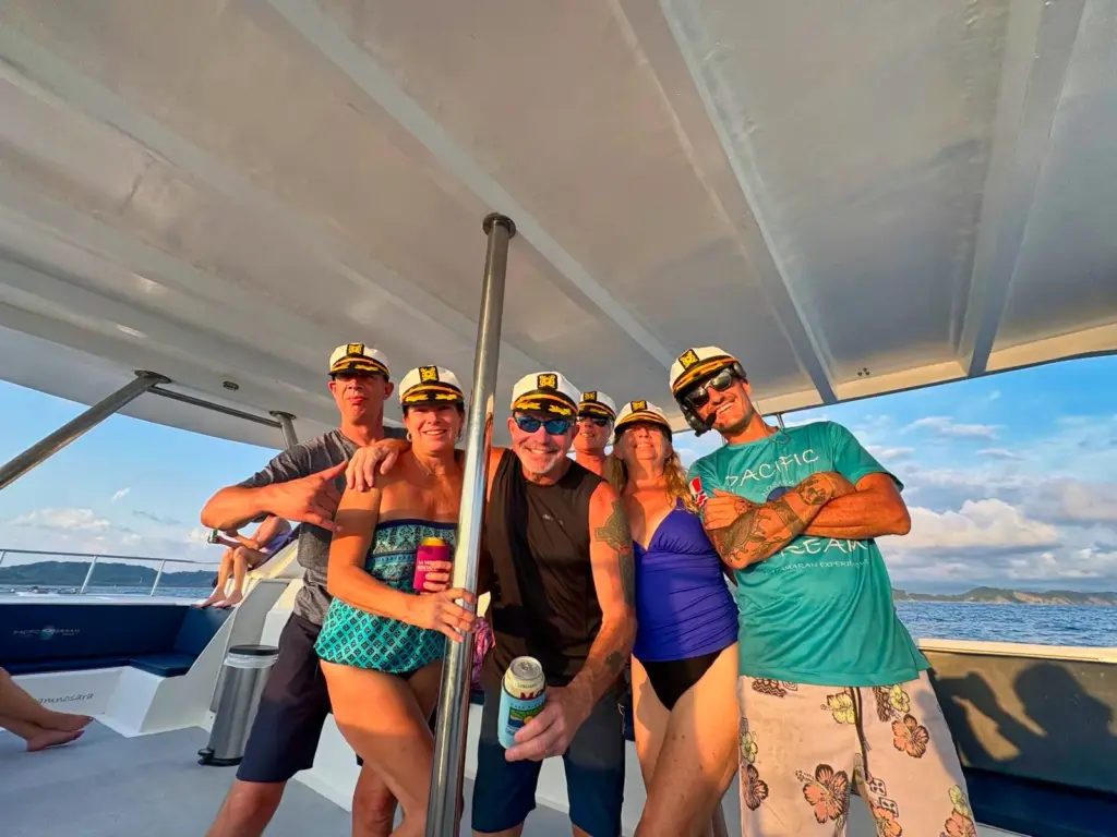 A group of guests in captain hats poses together on the boat's deck off the Nosara coast.