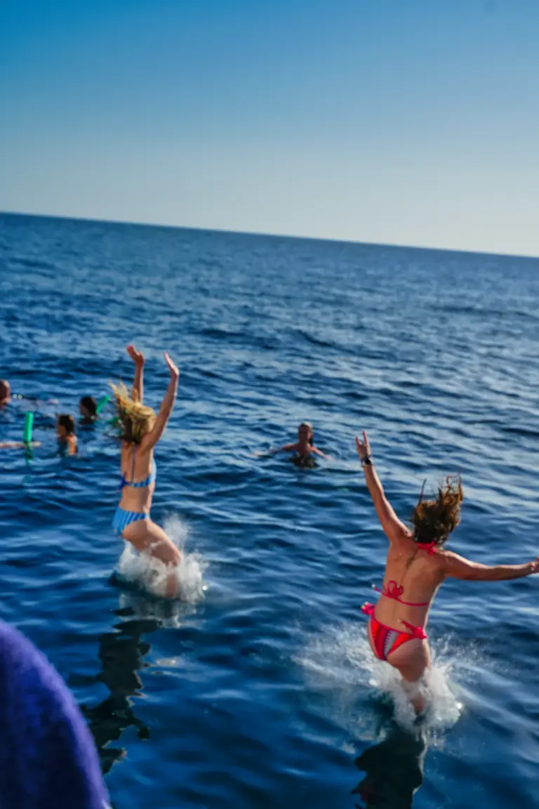 Two guests jump into the water together while others float nearby during a swim stop.