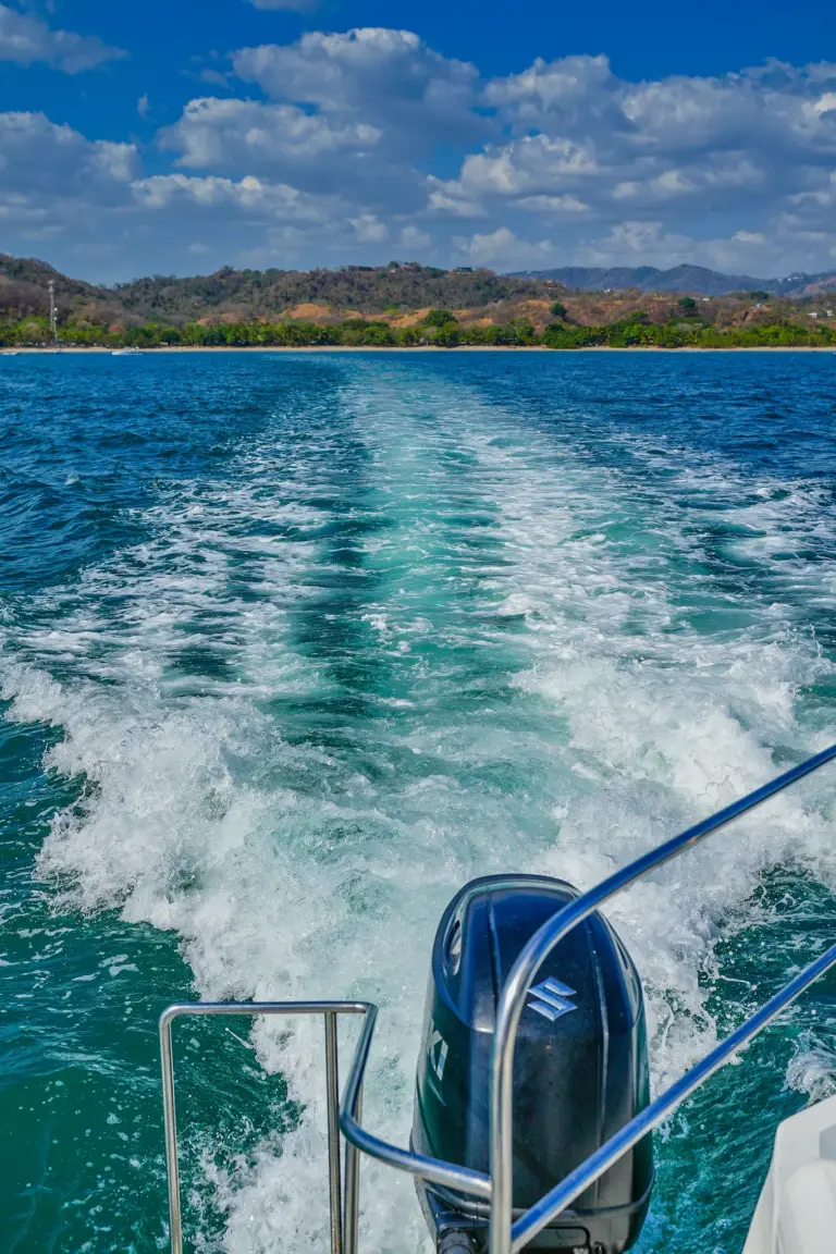 The boat's wake trails across turquoise water with the green Guanacaste coastline behind.