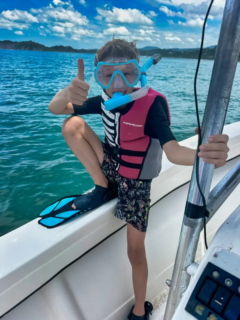 A young guest in a mask, snorkel and fins gives a thumbs up before jumping in off Nosara.