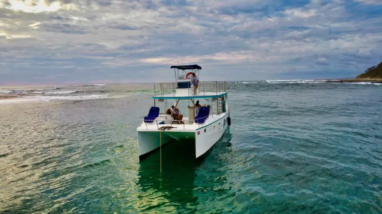 The catamaran sits anchored in clear green shallows beside a sandbar on the Nosara coast.
