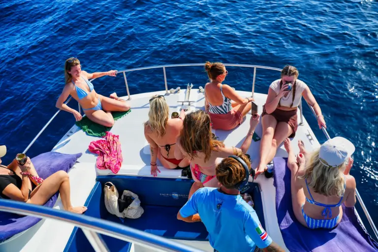 Guests fill the catamaran's bow, sunbathing and talking above deep blue water.