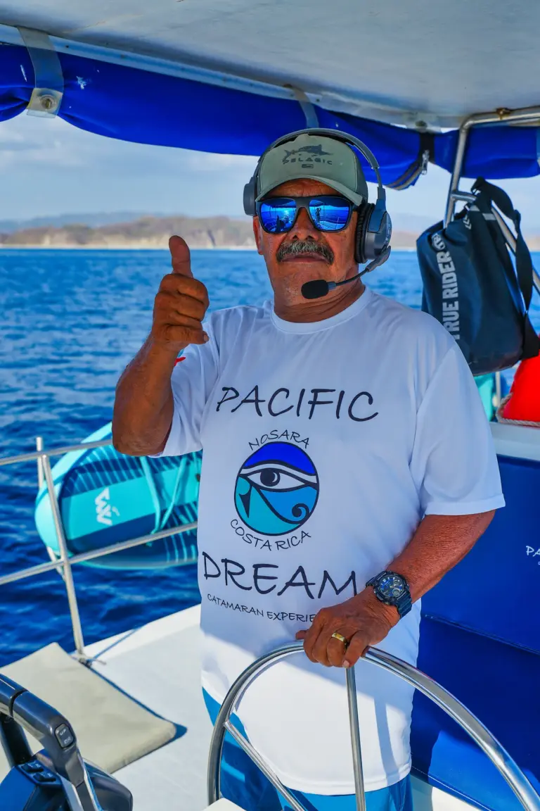 The captain gives a thumbs up from the wheel with the Nosara coastline behind him.