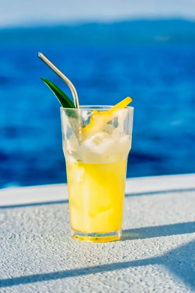A tall glass of fresh lemonade rests on the catamaran's rail above deep blue water.
