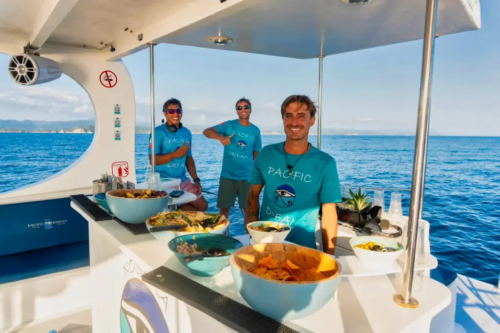 Three crew members stand behind the buffet of fresh salads, ceviche and nachos on deck.