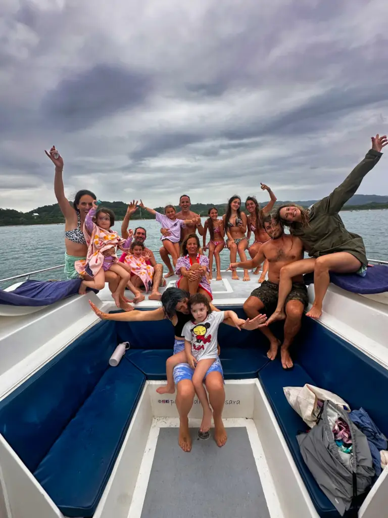 Families with children raise their arms and cheer on the catamaran's stern near the coast.