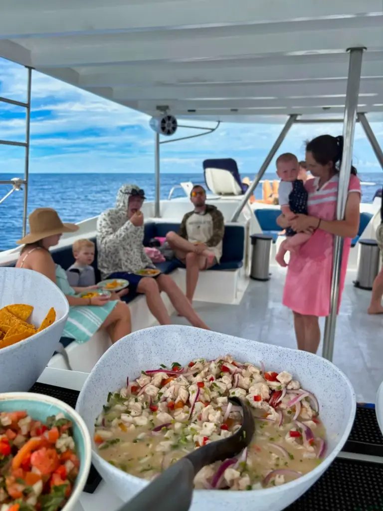 Families relax on the shaded catamaran deck while a large bowl of ceviche is served.
