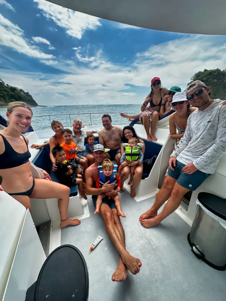 Families with small children in life jackets sit together on the catamaran's shaded deck.