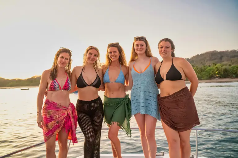 Five guests stand together on the catamaran deck with the green Nosara coastline behind.