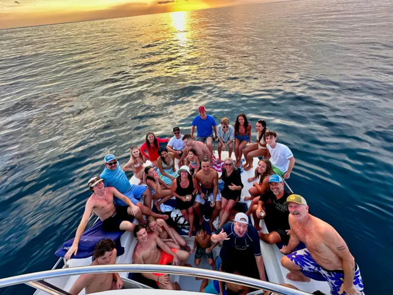 A large group fills the catamaran's bow as the sun lays a gold path across the water.