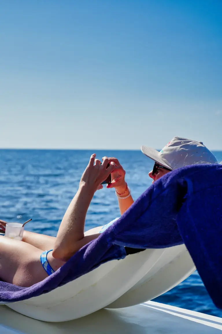 A guest lies on the catamaran's bow taking a photo of the open Pacific off Nosara.
