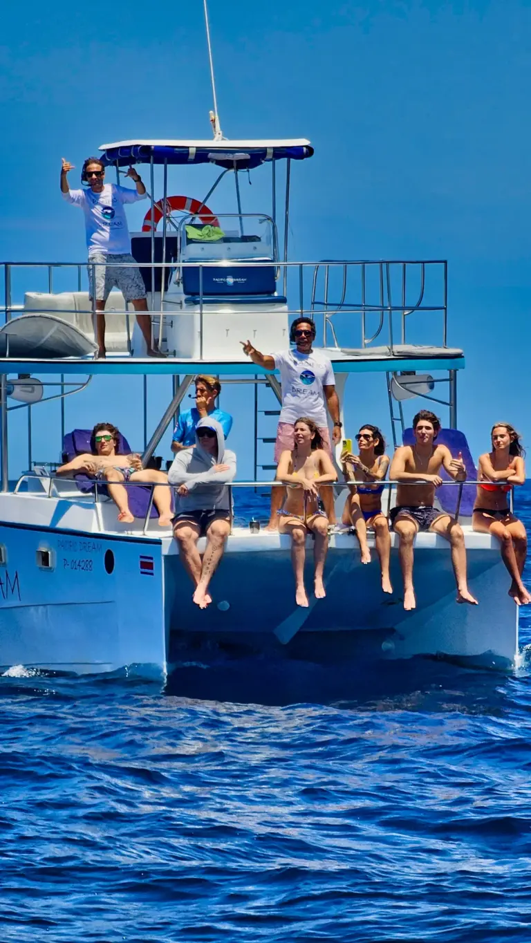 Guests sit with their feet over the side of the catamaran above deep blue water.