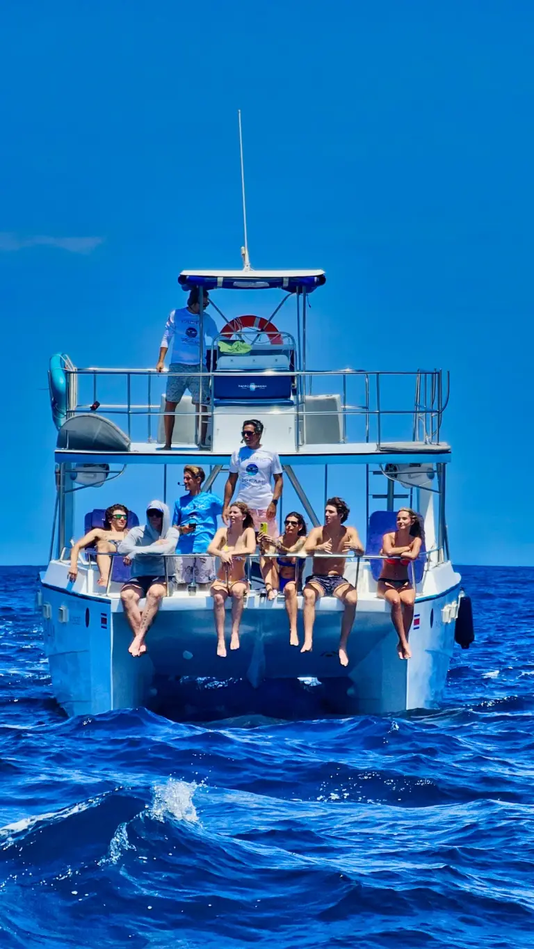 Guests sit along the catamaran's stern as it cruises across deep blue water off Nosara.
