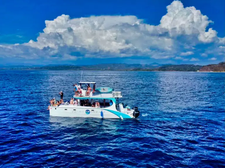 The catamaran cruises on deep blue water with big white clouds over the Guanacaste hills.