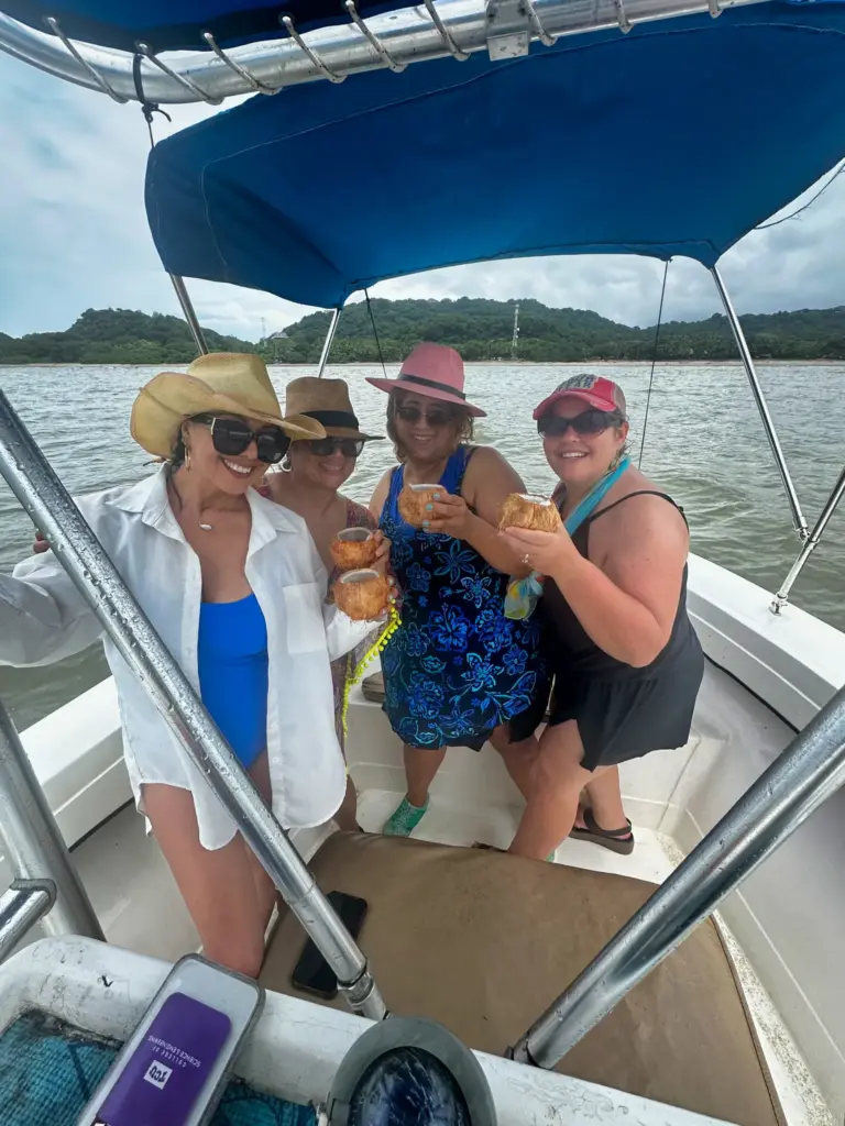 Four guests share drinks and snacks under the boat's shade canopy near the green Guanacaste coast.