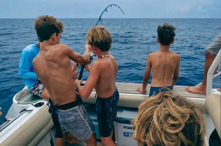 Three boys work a bent fishing rod together at the stern during a family trip from Nosara.