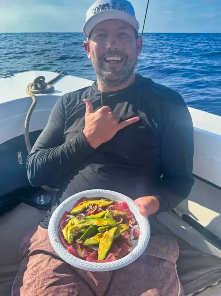 A guest holds a plate of fresh tuna and avocado prepared on board after a morning of fishing.