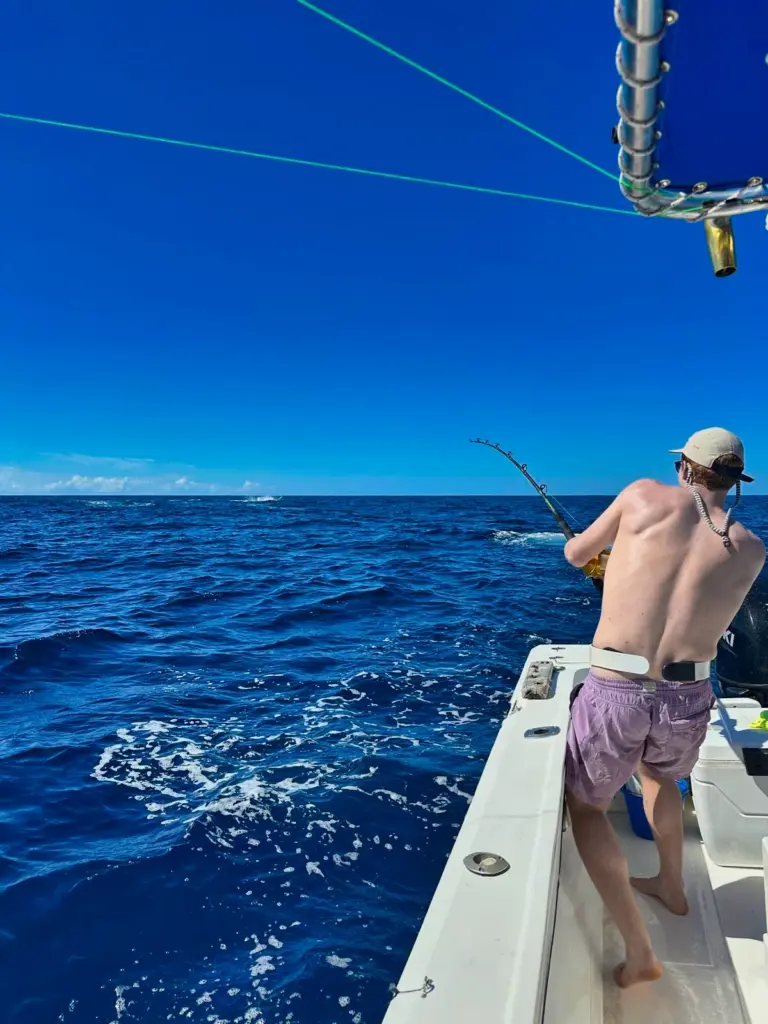 An angler leans into a bent rod at the rail with deep blue water and whitecaps behind.