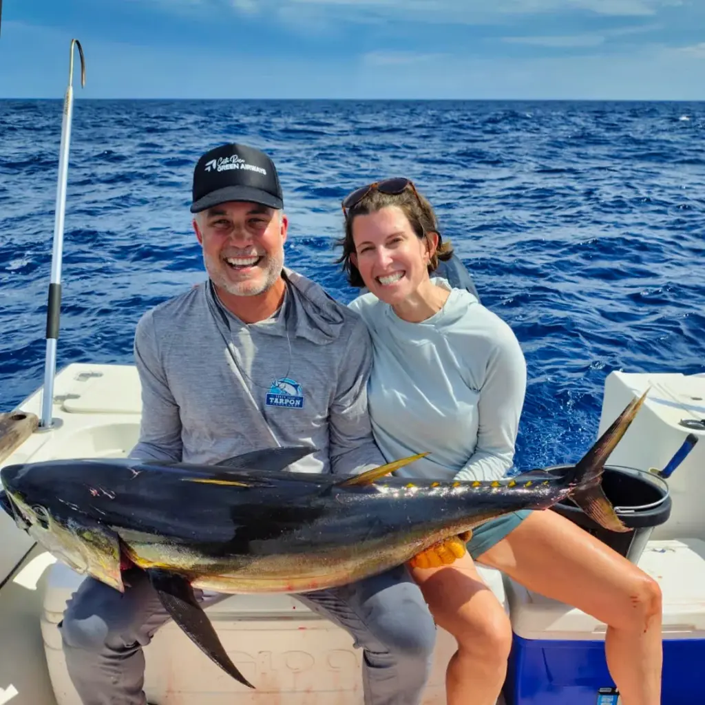 A couple holds a large yellowfin tuna across the gunwale in deep blue water off Nosara.