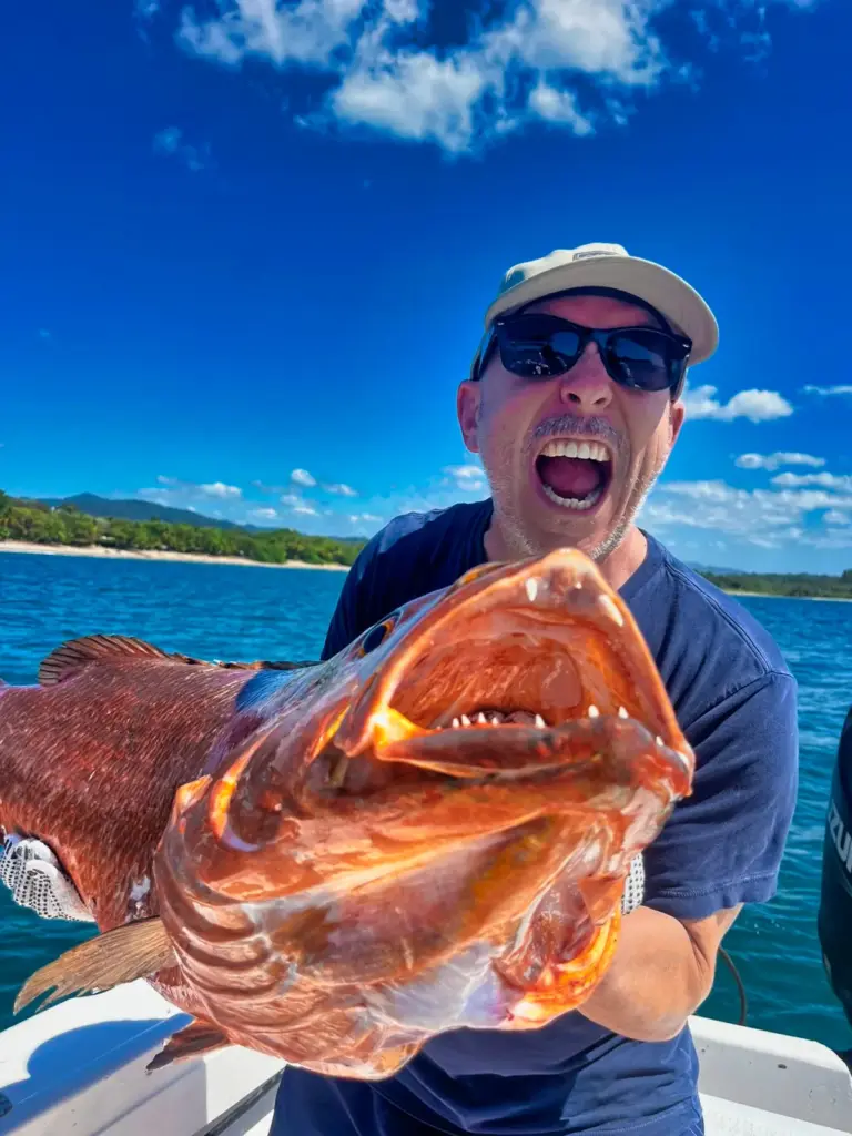 A guest holds up a large cubera snapper with the green Nosara coastline behind the boat.
