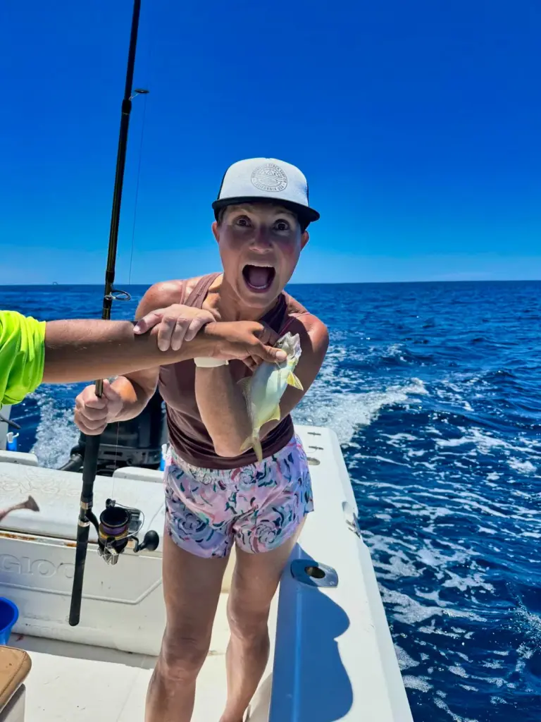 A guest cheers as a crew member passes her a fish at the stern with the wake behind.