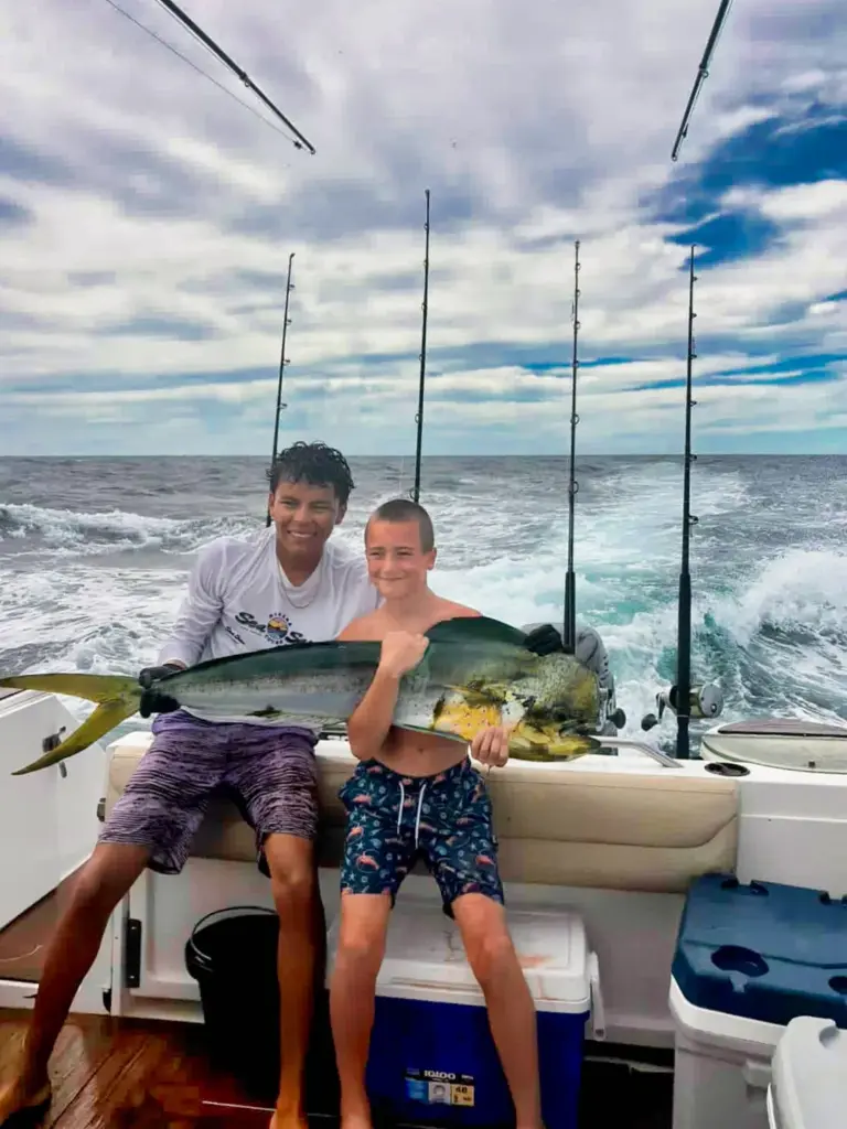 A crew member and a boy hold a roosterfish and a mahi-mahi at the stern off Nosara.