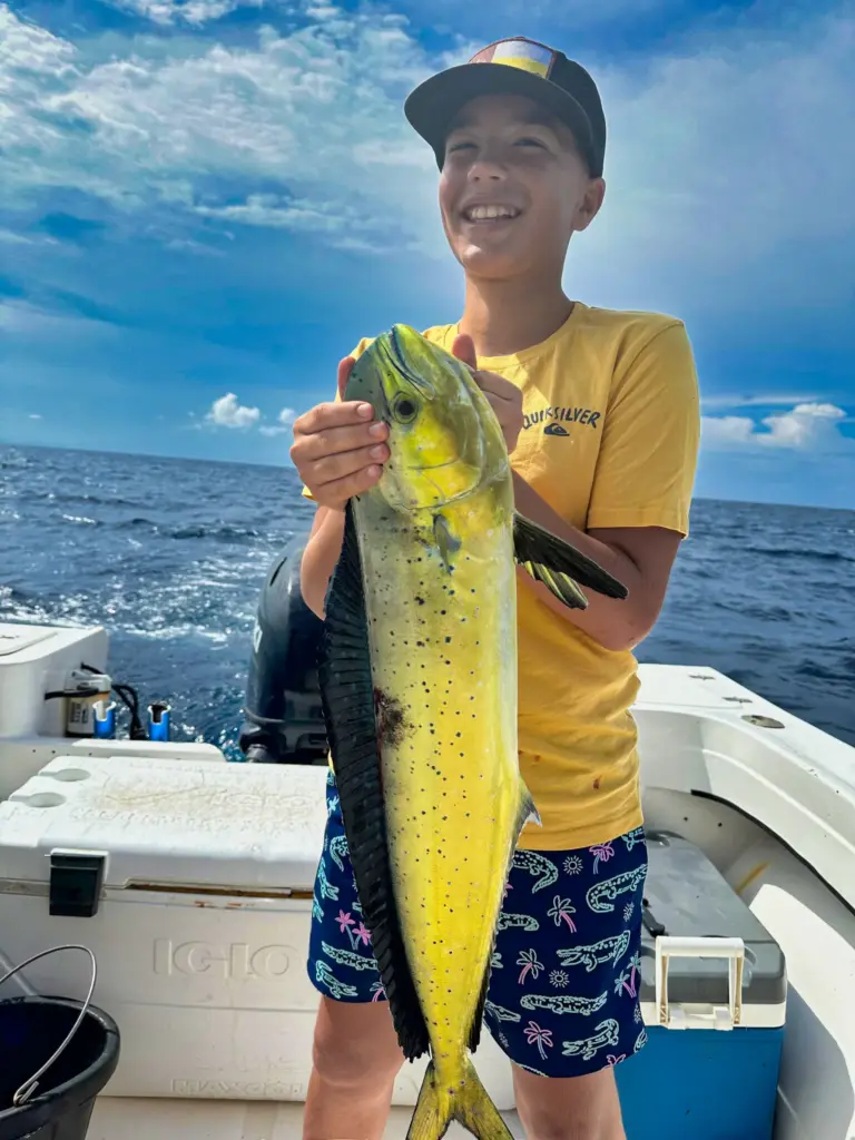 A young guest holds a bright yellow dorado on the deck after an inshore trip from Nosara.