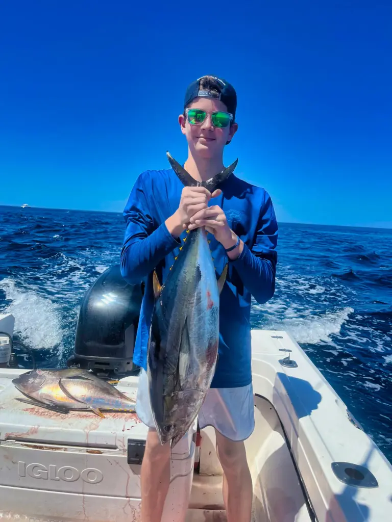 A guest holds a yellowfin tuna at the stern while the boat runs back toward Playa Garza.