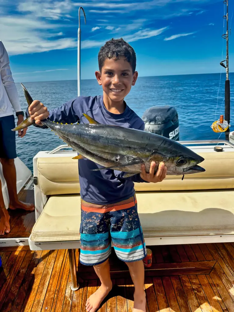 A young guest proudly holds a yellowfin tuna on the teak deck after an offshore trip.