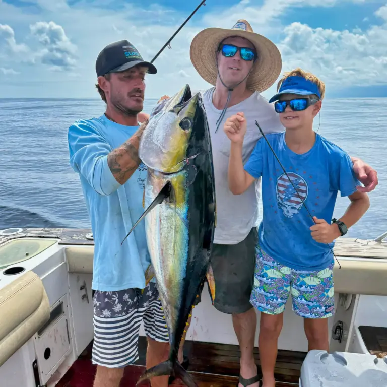 A crew member and two guests hold a large yellowfin tuna on the deck off Nosara.