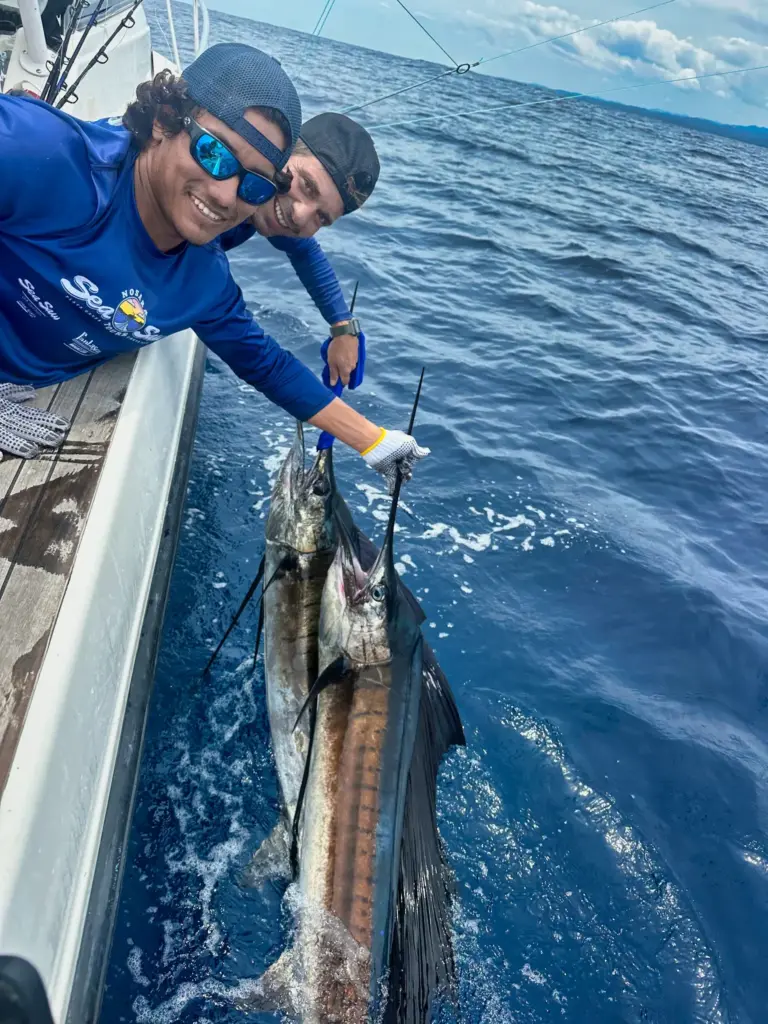 Crew members hold a sailfish in the water beside the boat during an offshore trip.