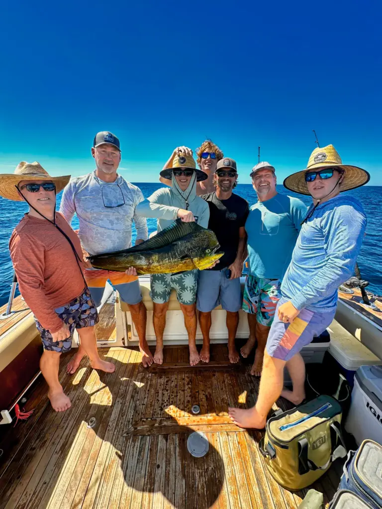 A group of guests holds up a mahi-mahi together on the boat's teak deck off Nosara.