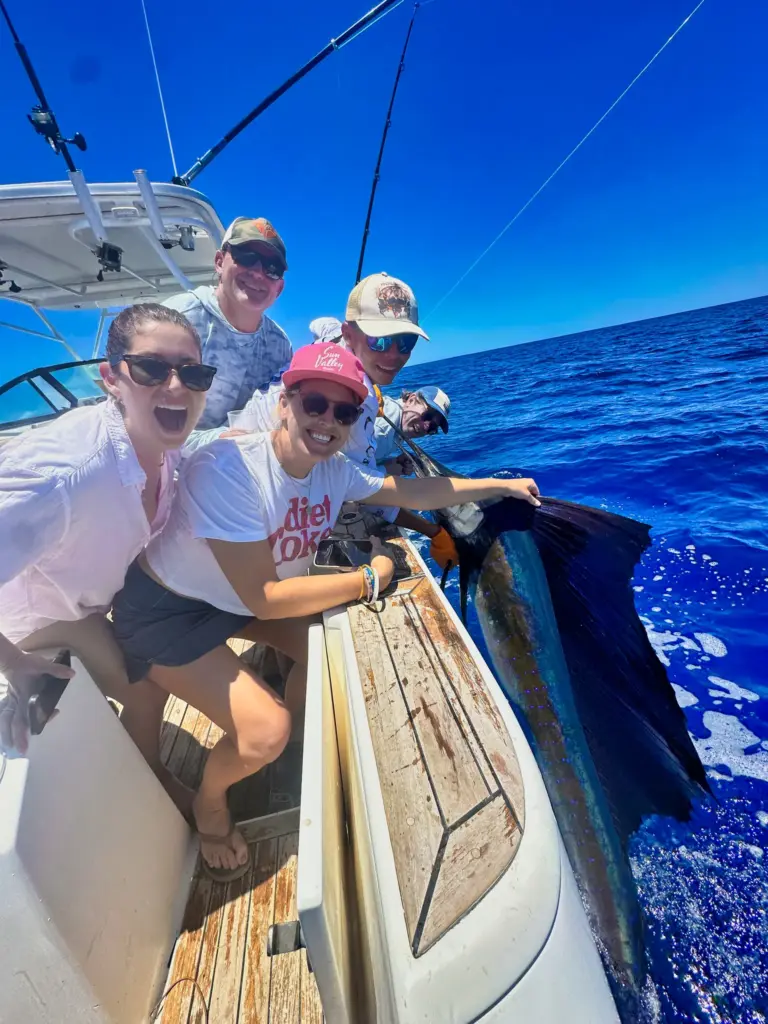 A group of guests crowds the transom to see a sailfish held in the water before release.
