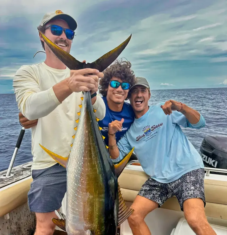 A guest holds a big yellowfin tuna while two crew members celebrate beside him.