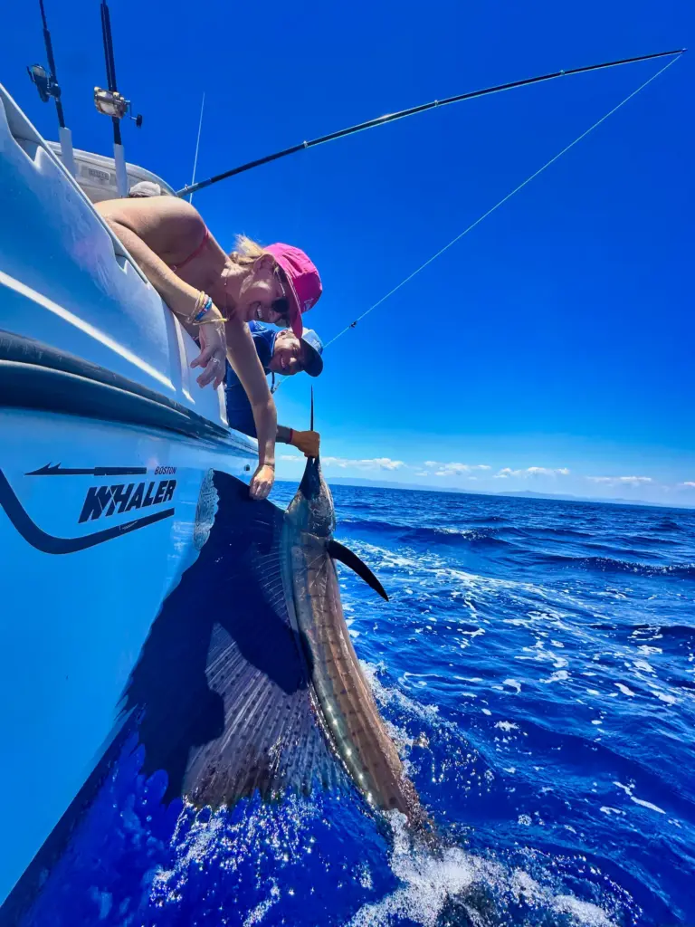 A guest leans out over the bow to release a sailfish back into the blue water off Nosara.