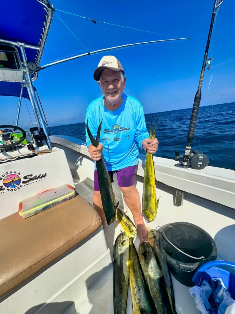 A guest holds two mahi-mahi over a deck full of fish after an offshore trip from Nosara.