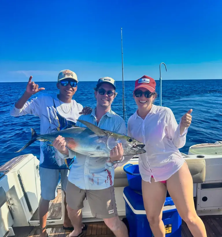 Guests and a crew member celebrate with a yellowfin tuna on the boat's teak deck.