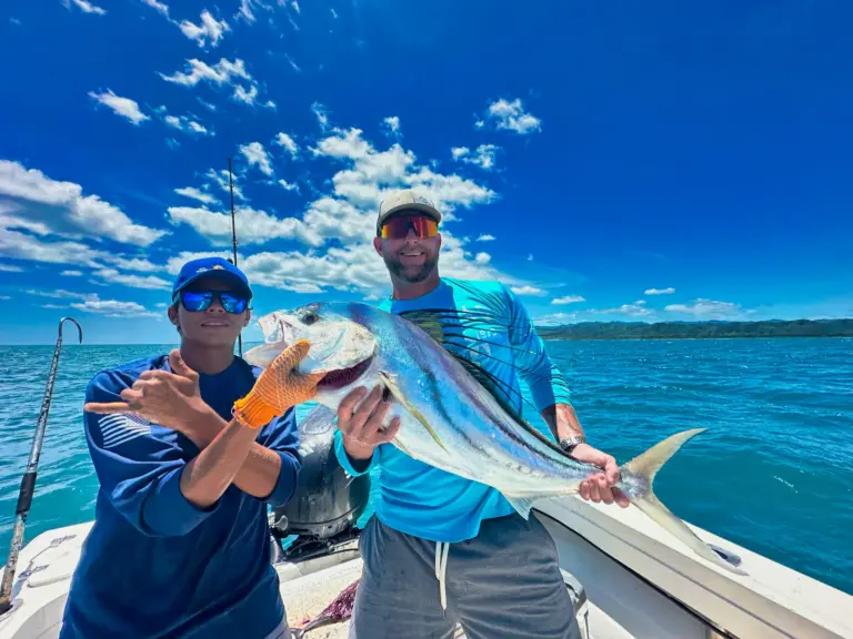 A crew member and a guest hold a mahi-mahi and a snapper with the coastline behind.