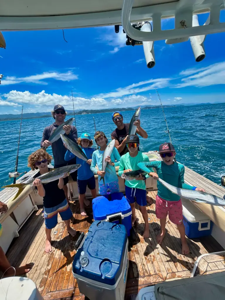A family group of children and adults holds up fish across the teak deck off Nosara.