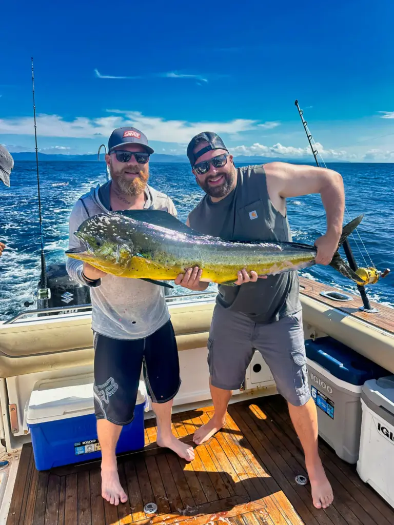 Two guests hold a bright mahi-mahi between them on the boat's teak deck off Nosara.