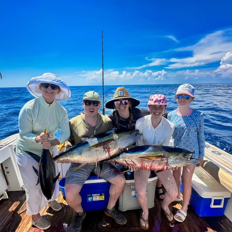 Five guests stand behind a row of yellowfin tuna laid across the coolers on deck.