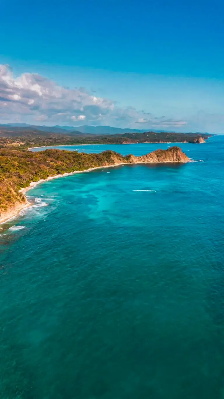 Aerial view of a long empty beach curving toward a green headland on the Guanacaste coast.