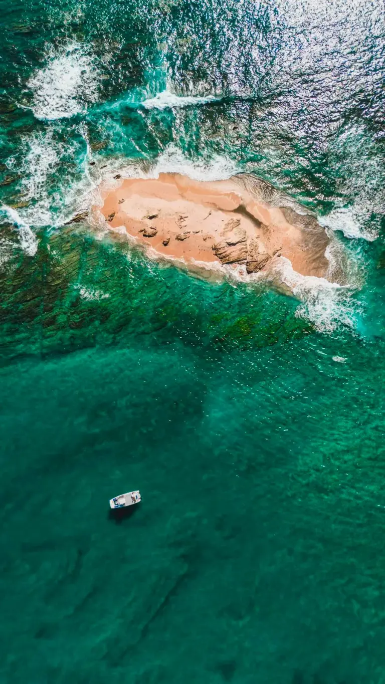 Aerial view of a boat anchored in clear green water beside the exposed sandbar near Nosara.
