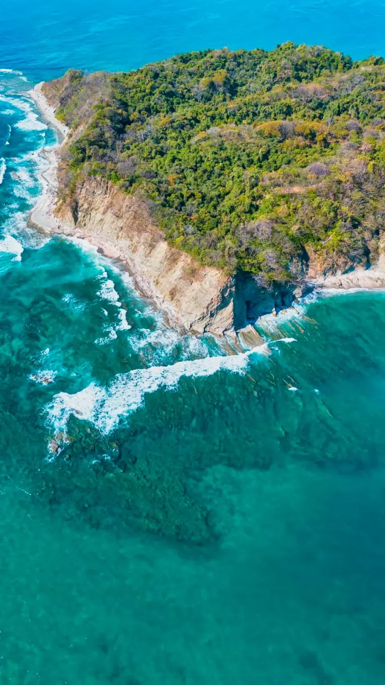 Aerial view of forested cliffs dropping to white surf and turquoise water near Nosara.